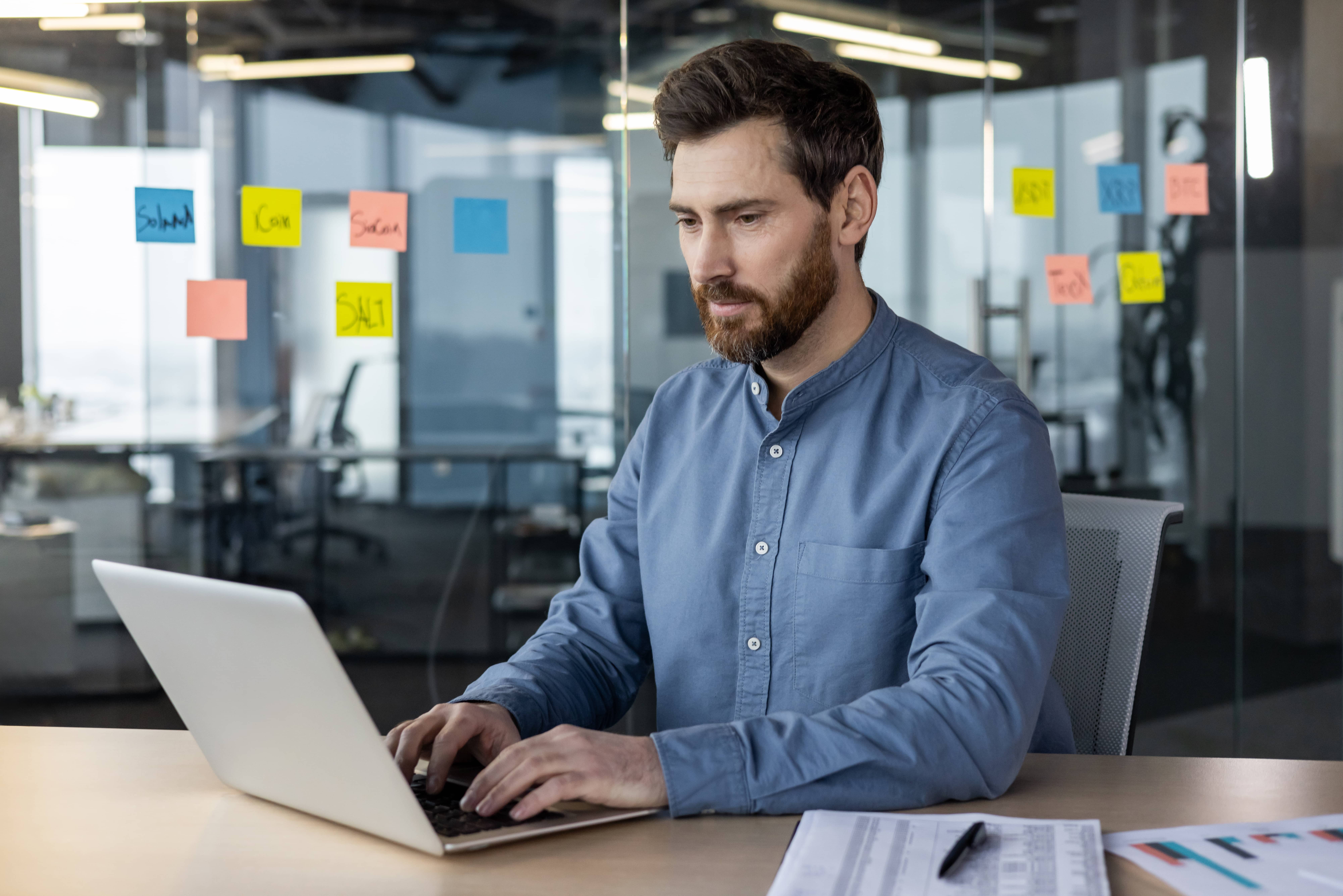 Business owner writing an email on laptop with notes and coffee