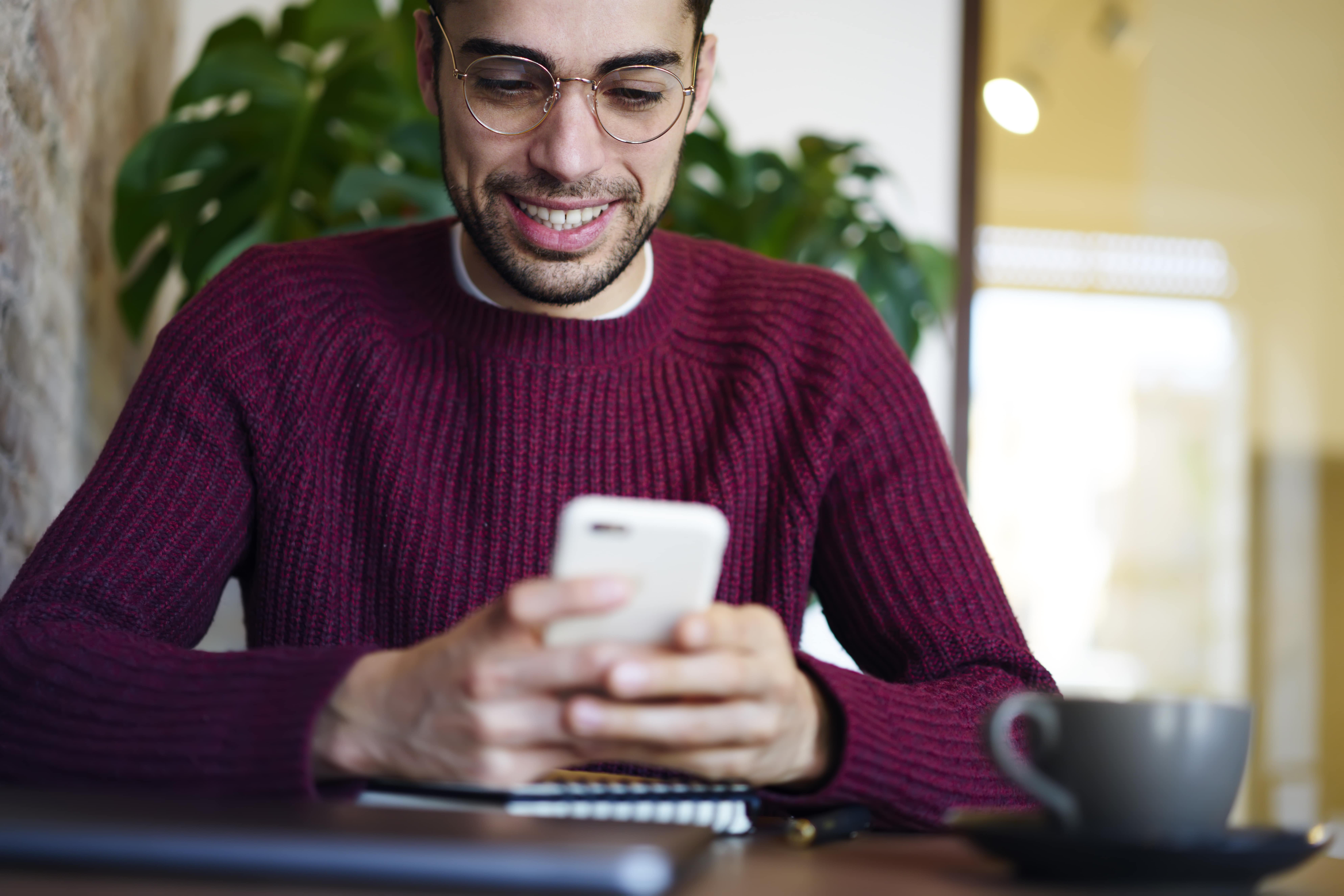 Person reading an email on their phone with a warm smile, cozy background